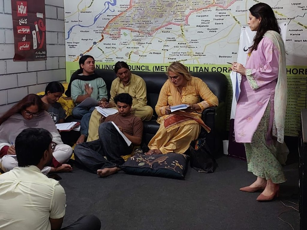 An instructor leading a Degardis session as participants take notes in a room with a map of Lahore
